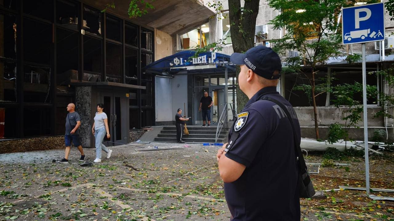Поліцейський біля пошкодженого офісного центру, люди прибирають уламки